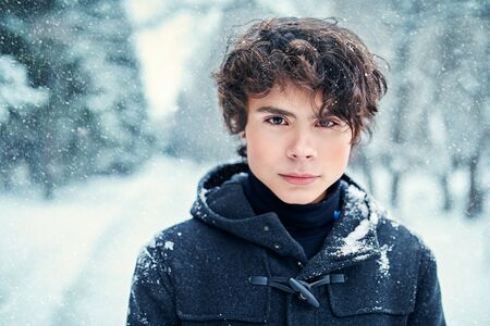 Handsome young man stands in a winter park under the snowfall. Winter season. Beauty, fashion.の写真素材