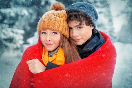 A young man and his girlfriend are standing, wrapped in a warm plaid, in a beautiful winter forest. Winter season, winter activities. First love.の写真素材