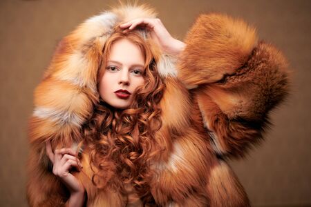 Fur coat style. Portrait of a beautiful sensual woman with red hair in a luxurious fox fur coat. Winter beauty fashion.の写真素材