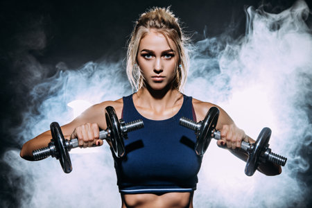 Muscular young woman with beautiful athletic body doing exercises with dumbbells. Fitness,...