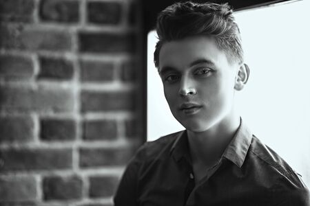 A monochrome portrait of a young guy in a shirt posing indoor. Fashion and beauty for men.の写真素材