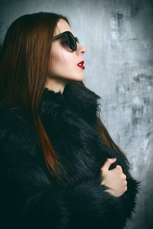A portrait of a beautiful gorgeous girl in black fur coat posing in the studio over the grunge background. Beauty, fashion.の写真素材