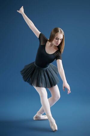 A full length portrait of an elegant refined ballet female dancer posing in the studio over the blue background. Talent, fashion for ballet dancers.の写真素材