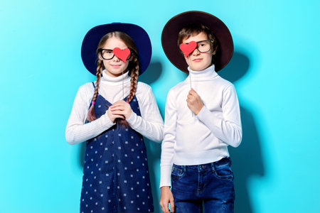 Happy pre-teen boy and girl holding two little hearts over blue background. Friendship. First love....