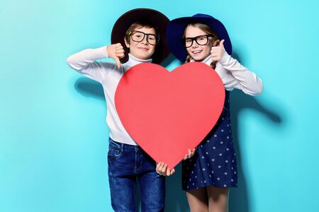 Happy pre-teen boy and girl holding big red heart over blue background. Friendship. First love. Valentine's Day.の写真素材