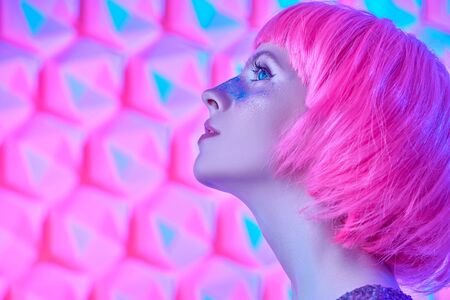 Portrait of a beautiful young girl with silver make-up posing in pink wig in a colorful blue and pink light. Party style. Beauty and fashion.の写真素材