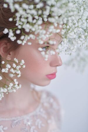 Beautiful tender girl with lovely freckles on her face and in a gypsophila wreath on a white background. Inspiration of spring and summer. Perfume, cosmetics concept. Prifile portrait.の写真素材