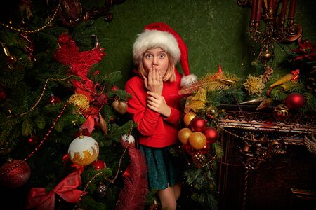 Funny mischievous girl hunts down Santa Claus, hiding behind a New Yearâs fireplace at home. Merry Christmas and Happy New Year!の写真素材