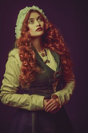 Portrait of a beautiful young woman with long red hair wearing medieval clothes on a dark violet background. Historical reconstruction of the Middle Ages.の写真素材