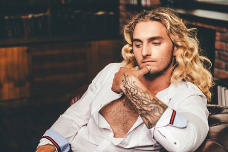 Handsome young man in white shirt lying on a sofa. Men's beauty, fashion. Hair, hairstyle.の写真素材