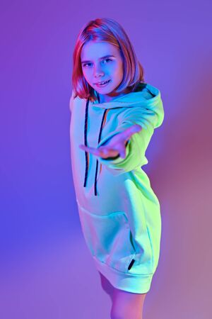 Modern girl teenager in sweatshirt posing at studio in bright color light. Youth style and fashion. Active lifestyle.の写真素材