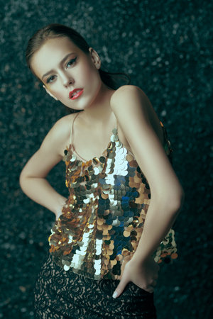 Makeup and cosmetics. Portrait of a gorgeous young woman with golden make-up on a dark grey...