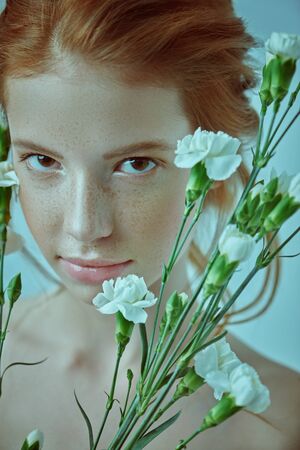 Beauty portrait of a tender young girl posing with white carnation flowers on a white background. Perfume, beauty cosmetics concept.の写真素材
