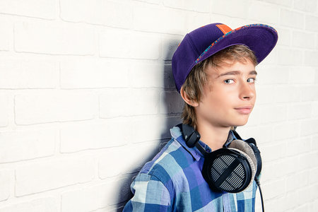 A portrait of a teenager posing with headphones against a white wall. Education, knowledge.