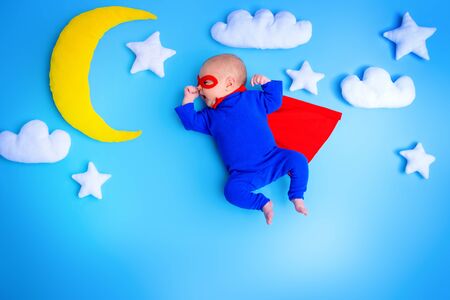 Little baby superhero with red cape flies through the night sky.の写真素材