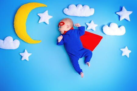 Little baby superhero with red cape flies through the night sky.の写真素材