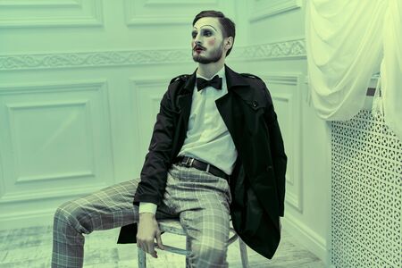 Art and fashion. A young man with makeup in the style of the 20s poses in an elegant suit in a classic vintage interior. Male mime artist.の写真素材