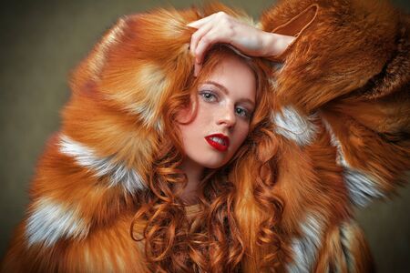 Fur coat style. Portrait of a beautiful sensual woman with red hair in a luxurious fox fur coat. Winter beauty fashion.の写真素材