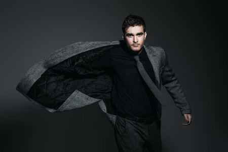 A portrait of a fashionable young man posing in movement in the studio over the grey background....