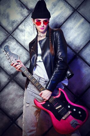 Rock musician girl with electric guitar on a grunge background. Urban rock style.の写真素材