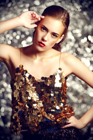 Make-up and cosmetics. Portrait of a gorgeous young woman with golden make-up on a sparkling silver...