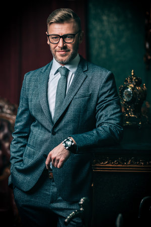 A portrait of a handsome mature man in a formal costume posing in the classic interior. Men's...