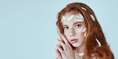 Portrait of a beautiful tender girl with white chrysanthemum petals on her face and body on a white background. Beauty, spa and cosmetics concept. Copy space.の写真素材