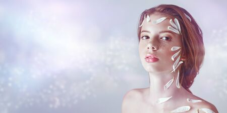 Portrait of a beautiful tender girl with white chrysanthemum petals on her face and body on a white background. Beauty, spa and cosmetics concept. Copy space.の写真素材