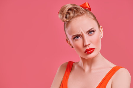 Pin-up beauty concept. Pretty blonde woman with make-up and hair in pin-up style stares at the...