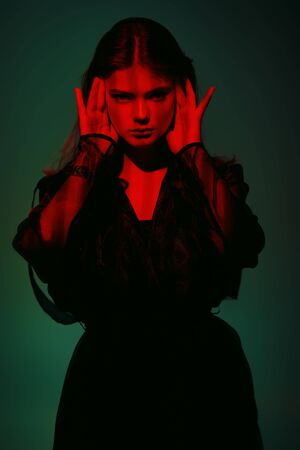 Fashion shot. Beautiful female model posing in black fashionable clothes in red light. Studio portrait.の写真素材