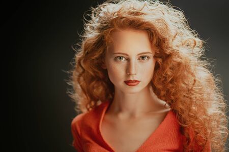 Beauty portrait. Charming girl with long red curly hair over black background. Hair care, hair coloring. Copy space.の写真素材