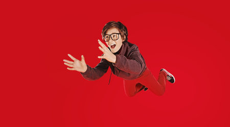 Educational concept. Happy schoolboy in glasses flies through the air and screams. Red background....