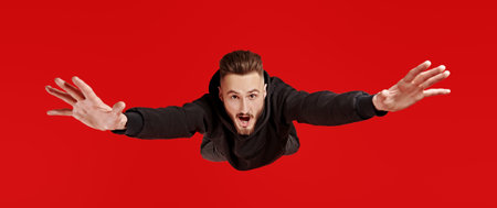Excited young man is flying through the air like a hero. Studio portrait on a red background.