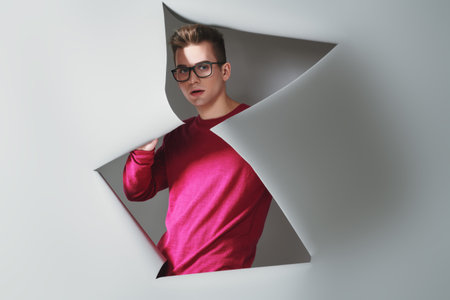Beauty, fashion concept. Modern young man in casual clothes and glasses posing at studio with grey...