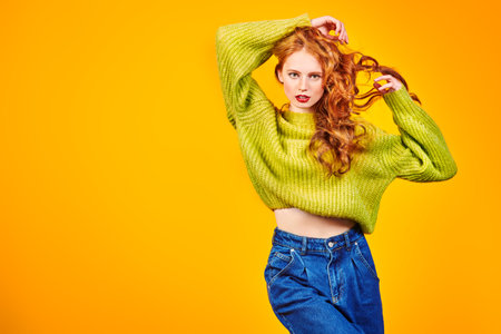 Fashion studio shot. Beautiful young girl with bright red hair posing at studio in modern casual...