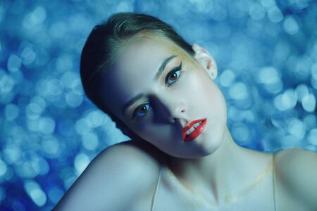 Make-up and cosmetics. Portrait of a gorgeous young woman with golden make-up on a sparkling blue background. Party style.の写真素材