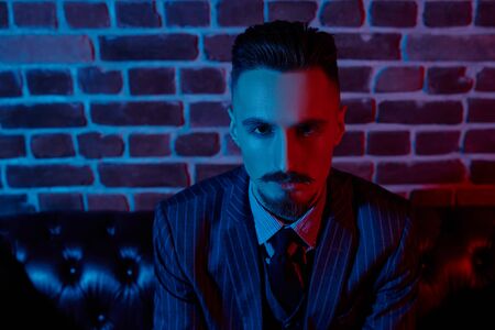 Portrait of a handsome young man in elegant suit standing in red light by a brick wall. Men's fashion. Luxurious lifestyle.の写真素材