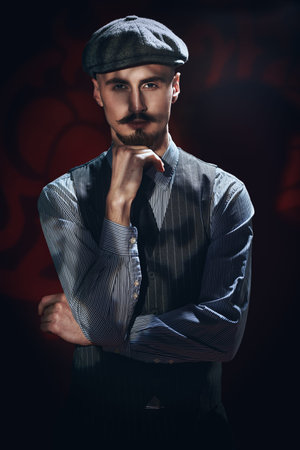 Portrait of a handsome man in elegant classical suit and a cap standing in the darkwith shadows...