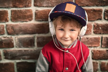 A portrait of a young schoolboy posing in the studio over the brick wall and listening to music in the headphones. Kids casual fashion, education.の写真素材