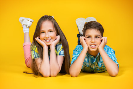 A portrait of two cheerful young kids over the yellow background. Summer casual kids fashion.