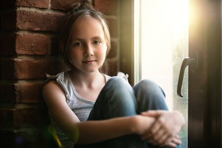 A portrait of a young cute girl over the window in a room. Beauty, summer casual fashion.の写真素材