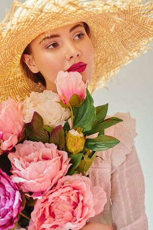 Beautiful romantic girl in a straw hat and with a bouquet of peonies happily smiles at the camera. Summer season. Beauty and cosmetics.の写真素材
