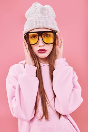 Bright teen girl in modern clothes and sunglasses on a pink background. Youth style, fashion. Studio portrait.の写真素材