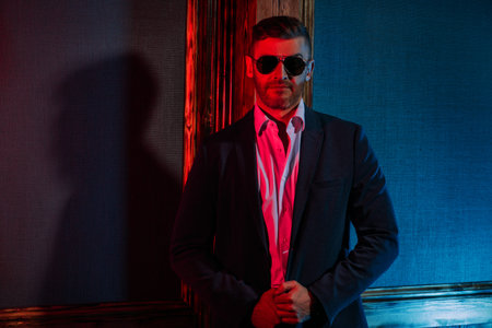 Portrait of a brutal handsome smiling man in sunglasses in blue and red light. Men's beauty,...