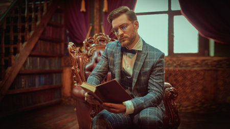 Handsome gentleman is sitting in a leather armchair  and reading a book in a vintage interior....