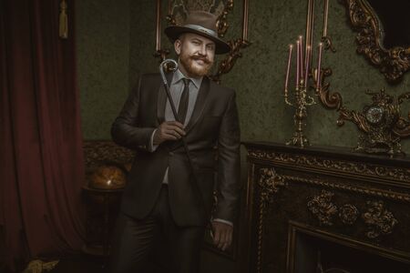 A portrait of an adult man with a stick posing in the vintage interior. Men's beauty, fashion, style.の写真素材