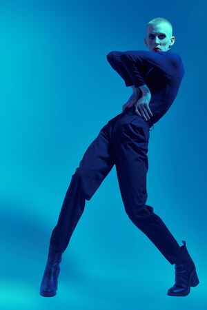 Full length portrait of a young man with womens makeup and in womens clothing posing at studio with expression. Avant-garde fashion.の写真素材