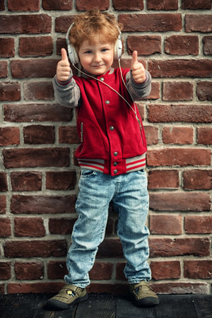 A full length portrait of a young schoolboy posing in the studio over the brick wall and listening...