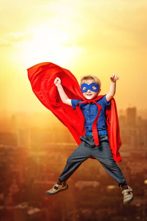 A full length portrait of a funny young boy flying in the costume of superhero. Kids development and education concept.の写真素材