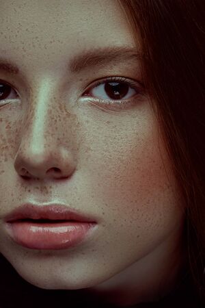 Close-up portrait of a beautiful young girl with freckles looking at camera. Studio portrait.の写真素材